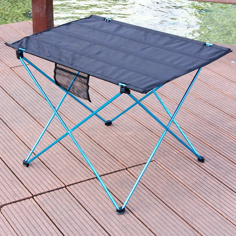 Load image into Gallery viewer, Foldable camping table with blue legs on a wooden deck by a body of water.
