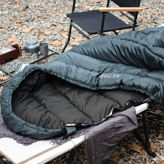 Green sleeping bag on a camping chair with a campfire and kettle in the background