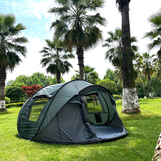 Green camping tent set up on grass with palm trees in the background