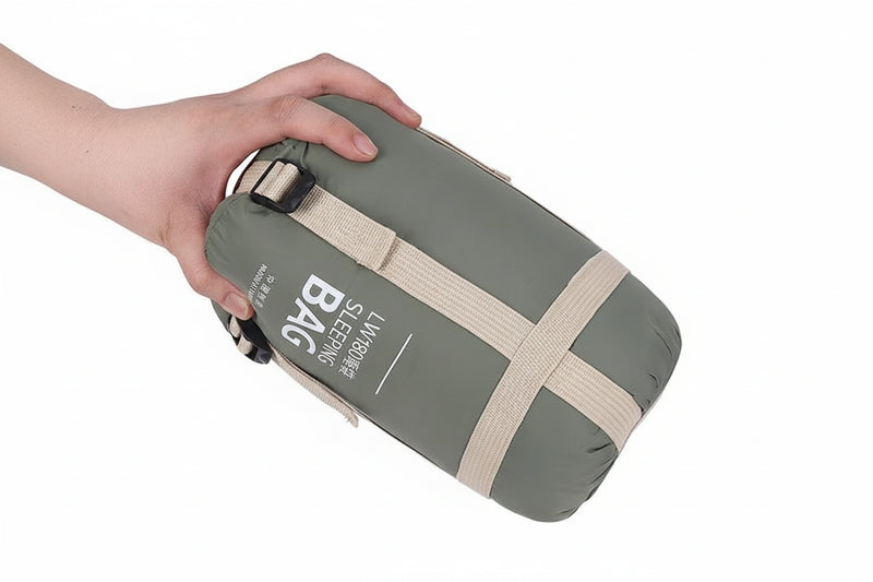 Load image into Gallery viewer, Hand holding a green sleeping bag with beige straps on a white background

