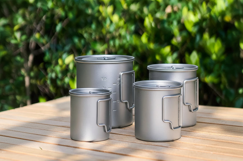 Load image into Gallery viewer, Set of metallic mugs with handles on a wooden surface against a green leafy background
