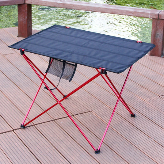 Foldable camping table with red legs on a wooden deck by a body of water