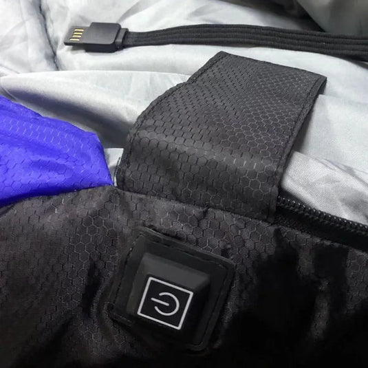 Close-up of a black heated glove with power button on a gray jacket background